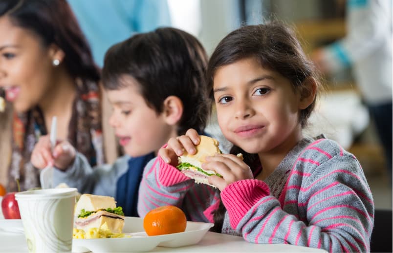 Two children eating sandwiches and fruit.
