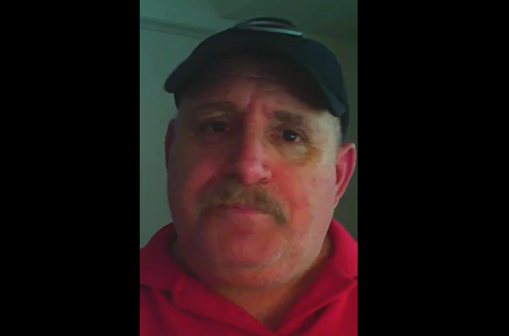 A headshot of a man wearing a baseball cap and a red collared shirt