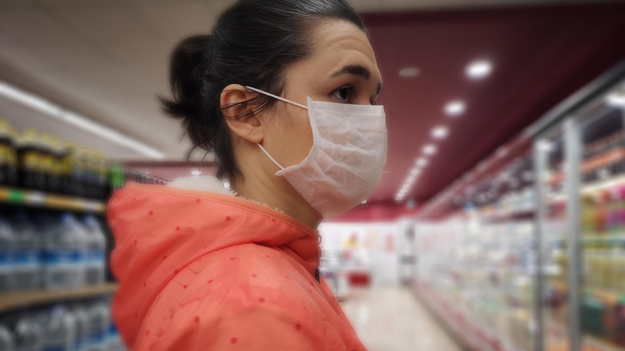 Young woman wears medical mask against virus while grocery shopping in supermarket,  health, safety and pandemic concept