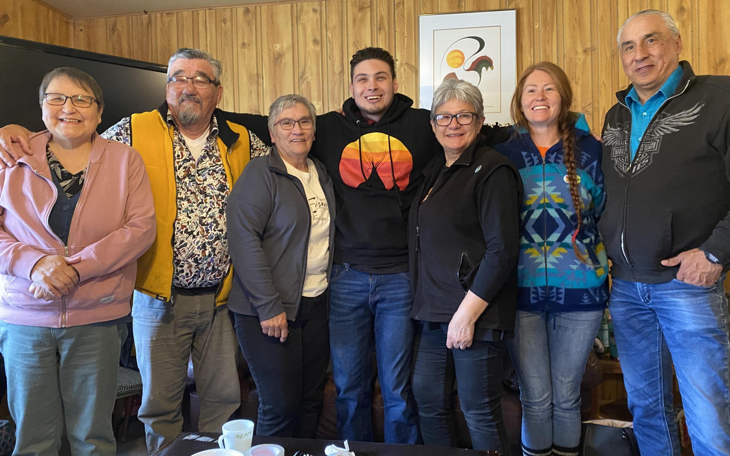 A group of Indigenous elders, smiling a the camera in a living room