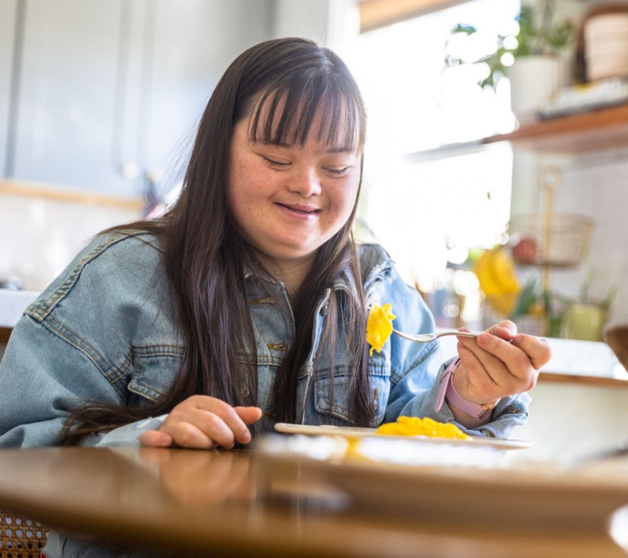 Girl with Downs syndrome disability eats breakfast at a kitchen table.
