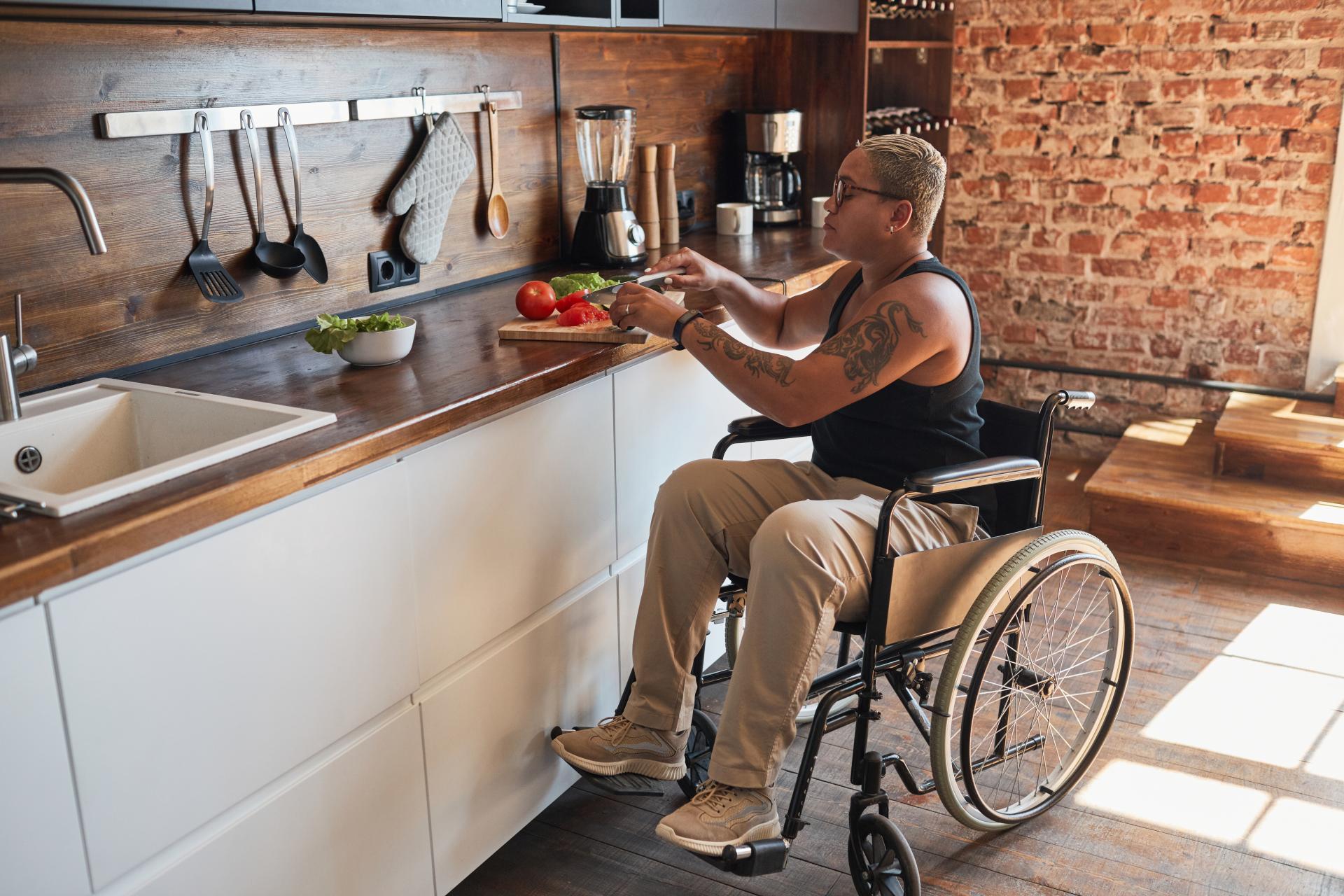 Young tattooed black woman in a wheelchair, cutting vegetables on a kitchen counter