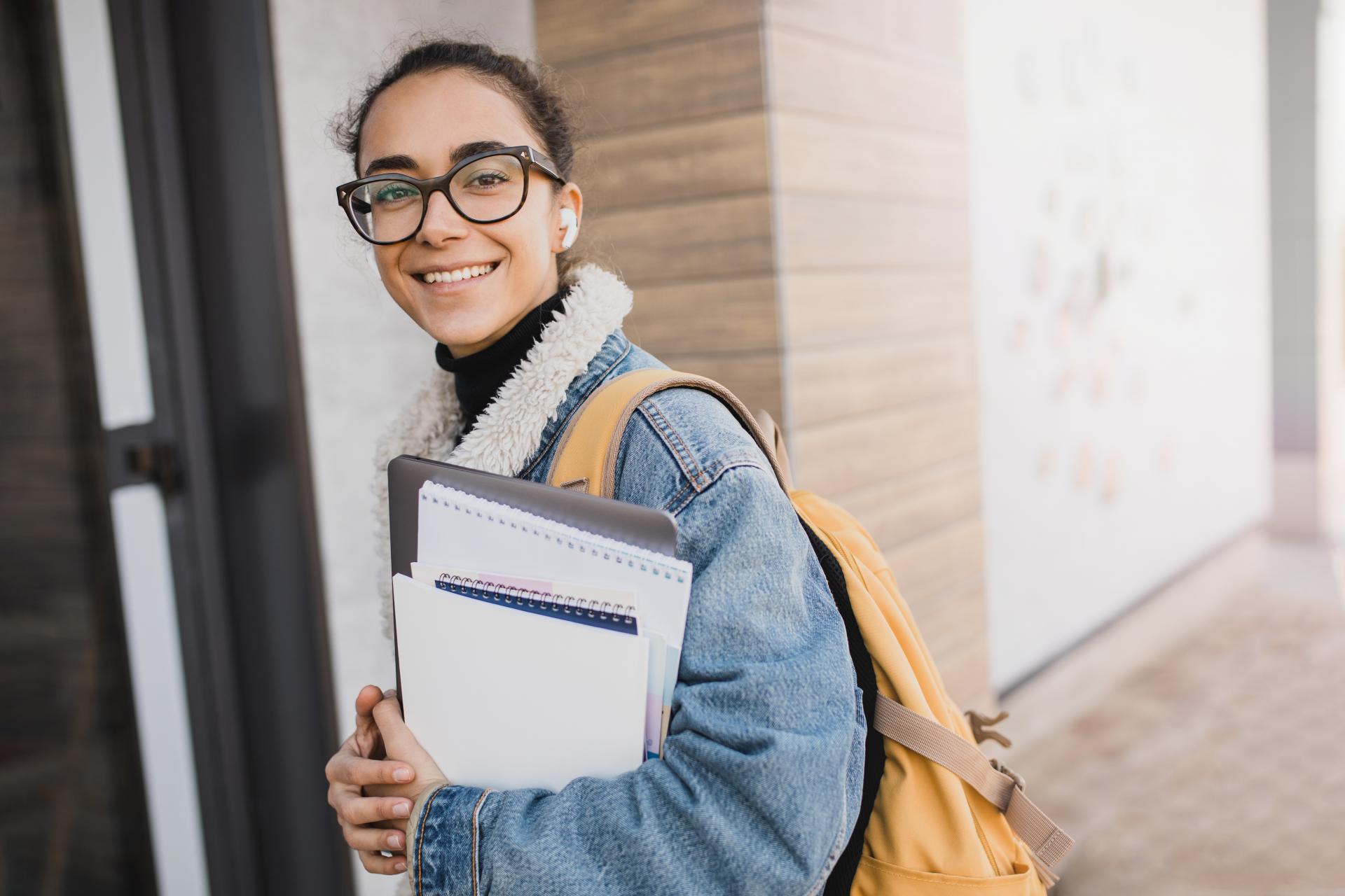 Young happy student with backpack standing near university holding books and laptop. Back to school.